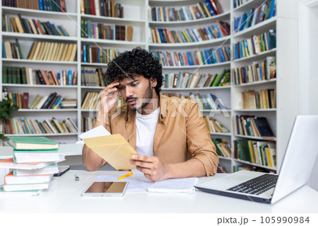 Young hispanic student upset studying inside university campus academic library, disappointed and sad received a letter with bad results in studies and entrance exam. Young hispanic student upset studying inside university campus academic library, disappointed and sad received a letter with bad results in studies and entrance exam. 105990984