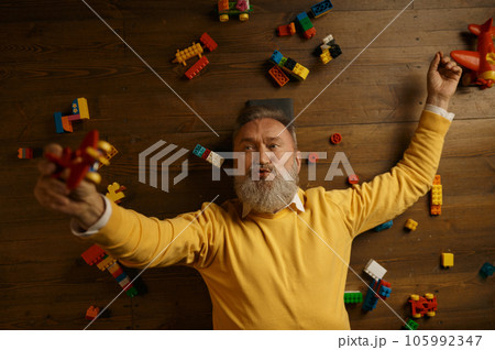 Happy senior man lying on floor with scattered toy building blocks 105992347