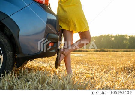 Young woman driver legs in yellow summer dress standing near her car enjoying warm summer day at sunset. 105993409