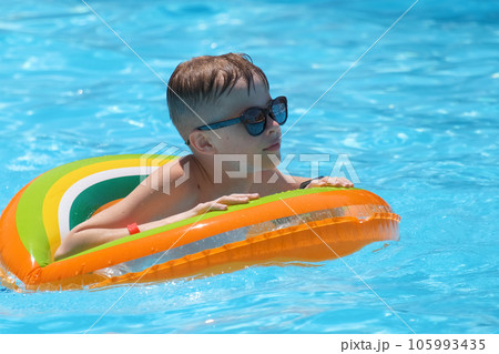 Young joyful child boy having fun swimming in inflatable air circle in swimming pool with blue water on warm summer day on tropical vacations. Summertime activities concept 105993435