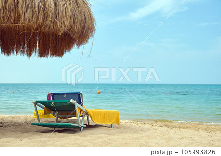 Straw shade umbrellas on sea tropical beach with resting sunbeds against blue vibrant sky in summer Straw shade umbrellas on sea tropical beach with resting sunbeds against blue vibrant sky in summer 105993826