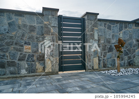 Stone high fence with shut iron door in paved yard of modern style design property outdoor 105994245