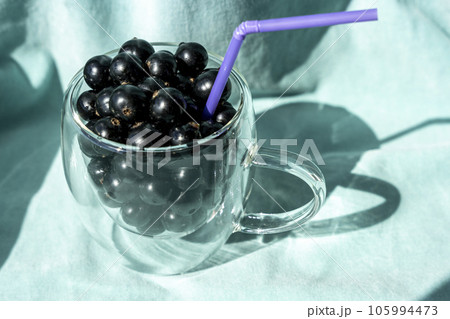 Summer fresh black currant berries in a glass mug with a cocktail tube Summer fresh black currant berries in a glass mug with a cocktail tube 105994473