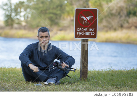 Drone operator is disappointed because he isn't allowed to fly his quadcopter in national park no drone area. Man is unable to use his UAV near restriction notice sign. Airspace use regulations 105995282