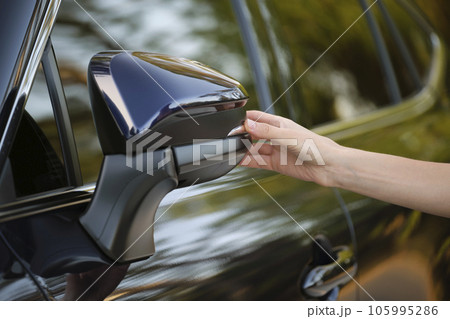 Driver hands adjusting side view mirror of a car 105995286