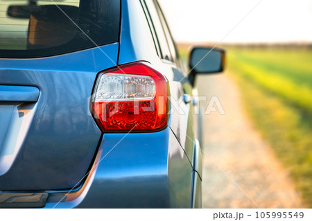 Closeup of rear red taillight and mirror of new clean blue SUV off-road car on rural road Closeup of rear red taillight and mirror of new clean blue SUV off-road car on rural road 105995549