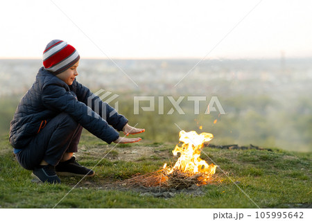Child boy warming near bonfire outdoors in cold weather. 105995642