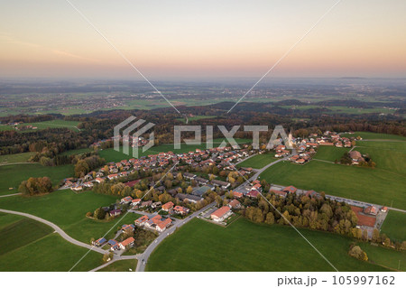 Aerial view of small town with red tiled roofs among green farm fields and distant forest in summer. 105997162