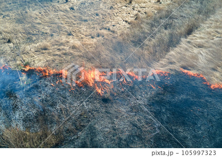 Aerial view of grassland field burning with red fire during dry season. Natural disaster and climate change concept Aerial view of grassland field burning with red fire during dry season. Natural disaster and climate change concept 105997323