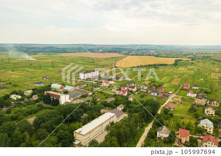 Aerial landscape view of village houses and distant green cultivated agricultural fields with growing crops on bright summer day Aerial landscape view of village houses and distant green cultivated agricultural fields with growing crops on bright summer day 105997694