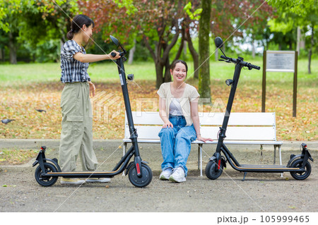 電動キックボードで会い、楽しく会話する若い女性｜電動キックボードイメージ 105999465
