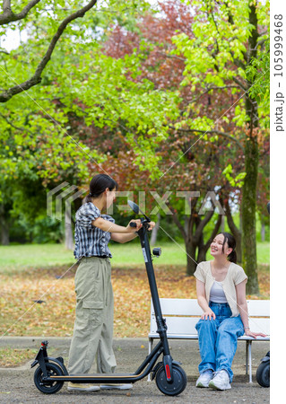 電動キックボードで会い、楽しく会話する若い女性｜電動キックボードイメージ 105999468