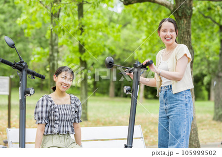 電動キックボードで会い、楽しく会話する若い女性|電動キックボードイメージ 電動キックボードで会い、楽しく会話する若い女性|電動キックボードイメージ 105999502