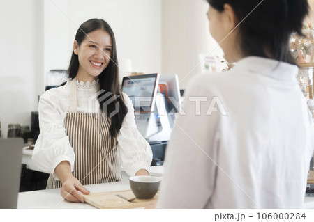 Smiling friendly barista serving  a cup of coffe to customer at coffee shop. 106000284