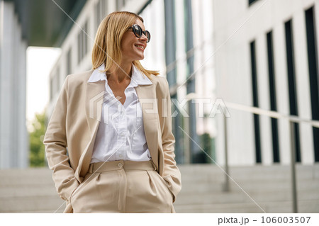 Stylish female entrepreneur is standing on office building background and looking at side 106003507