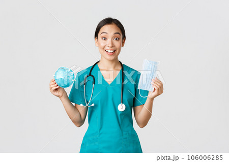 Covid-19, coronavirus disease, healthcare workers concept. Amused smiling asian female nurse, inters in scrubs showing respirator and medical mask, receive personal protective equipment Covid-19, coronavirus disease, healthcare workers concept. Amused smiling asian female nurse, inters in scrubs showing respirator and medical mask, receive personal protective equipment 106006285