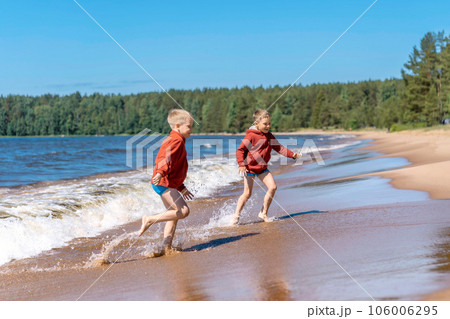 cute caucasian boys wearing red hoodies and blue underpants running from waves in Ladoga lake with enthusiasm cute caucasian boys wearing red hoodies and blue underpants running from waves in Ladoga lake with enthusiasm 106006295