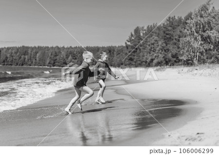 cute caucasian boys wearing red hoodies and blue underpants running from waves in lake with enthusiasm. cute caucasian boys wearing red hoodies and blue underpants running from waves in lake with enthusiasm. 106006299