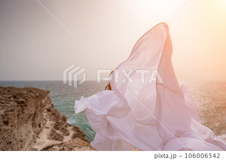 Woman sea white dress. Happy freedom woman on the beach enjoying and posing in white dress. Rear view of a girl in a fluttering white dress in the wind. Holidays, holidays at sea. Woman sea white dress. Happy freedom woman on the beach enjoying and posing in white dress. Rear view of a girl in a fluttering white dress in the wind. Holidays, holidays at sea. 106006542