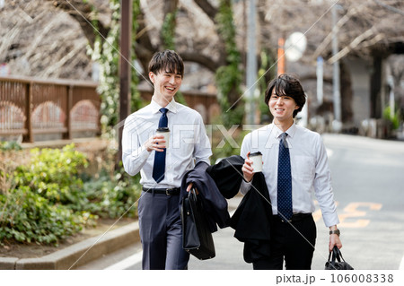 会話しながらテイクアウトカップを持って歩く2人の若いビジネスマンの男性 会話しながらテイクアウトカップを持って歩く2人の若いビジネスマンの男性 106008338
