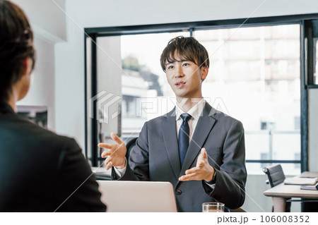 オフィスで対面の人物に説明とプレゼンテーションをする若いビジネスマンの男性 オフィスで対面の人物に説明とプレゼンテーションをする若いビジネスマンの男性 106008352