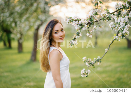 A young happy woman walks through an apple orchard among spring white flowers 106009414