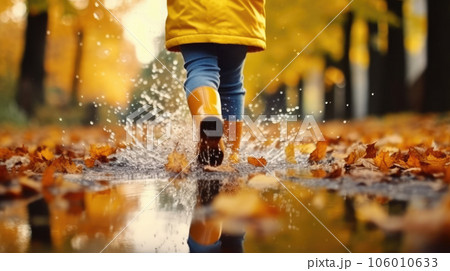 Children's feet in yellow rubber boots walk through a puddle. 106010633