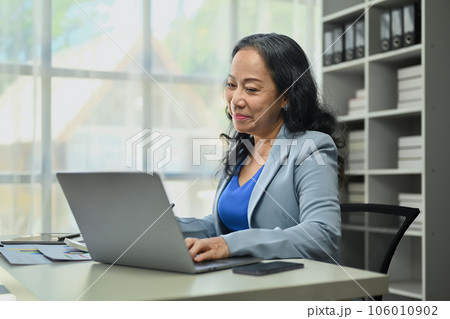 Beautiful mature businesswoman using laptop working with statistics documents at modern office. Beautiful mature businesswoman using laptop working with statistics documents at modern office. 106010902