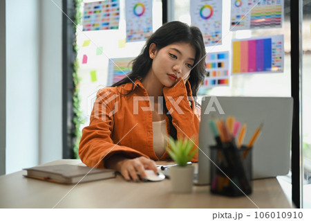 Bored, tired young woman looking at laptop while sitting at desk in creative office. Bored, tired young woman looking at laptop while sitting at desk in creative office. 106010910