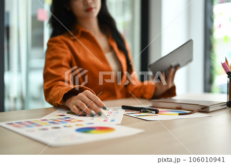 Select focus on woman hand choosing colors from color swatch samples and using digital tablet at workstation. 106010941