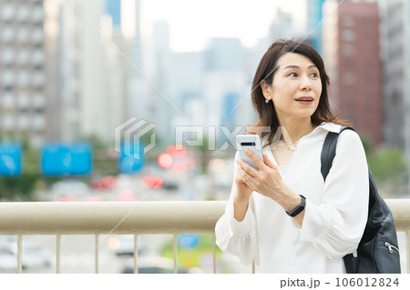 スマホで地図を見ながら、周りを確認しているアラフィフのビジネスウーマン スマホで地図を見ながら、周りを確認しているアラフィフのビジネスウーマン 106012824