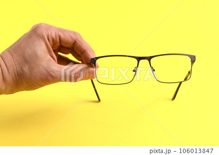 Hand holding plastic black glasses, isolated on yellow background. 106013847