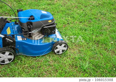 Lawn mower cutting grass. Small grass cuttings fly out of lawnmower. Grass clippings get spewed out of a mower pushed around by landscaper. CloseUp. Gardener working with mower machine. Mowing lawns 106015308