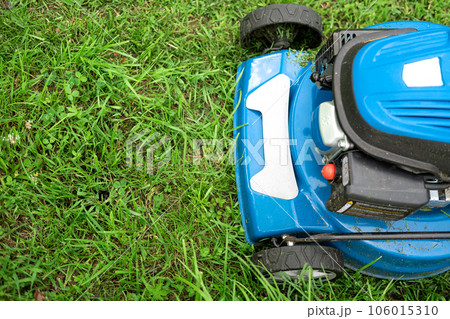Lawn mower cutting grass. Small grass cuttings fly out of lawnmower. Grass clippings get spewed out of a mower pushed around by landscaper. CloseUp. Gardener working with mower machine. Mowing lawns Lawn mower cutting grass. Small grass cuttings fly out of lawnmower. Grass clippings get spewed out of a mower pushed around by landscaper. CloseUp. Gardener working with mower machine. Mowing lawns 106015310