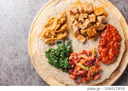 Ethiopian Injera flat bread with various vegetable and meat fillings close up on the wooden board. Horizontal top view Ethiopian Injera flat bread with various vegetable and meat fillings close up on the wooden board. Horizontal top view 106017658
