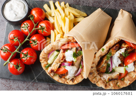 Greek fast food gyros with chicken, tomatoes, cucumbers and onions served with tzatziki sauce and french fries close-up on a board. Horizontal top view Greek fast food gyros with chicken, tomatoes, cucumbers and onions served with tzatziki sauce and french fries close-up on a board. Horizontal top view 106017681