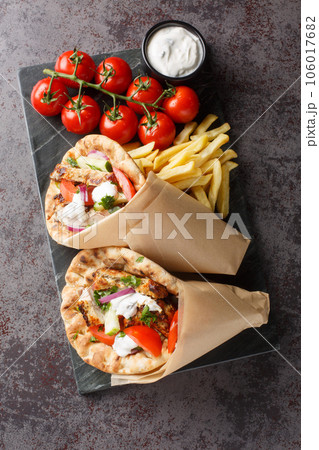 Greek gyros with chicken and fresh vegetables served with tzatziki sauce and french fries close-up on a board. Vertical top view 106017682