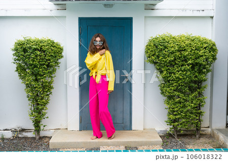 Stylish fit fashion women in bright pink wide leg pants and yellow shirt holding bag trendy mint sunglasses posing at luxury tropical villa by pool outdoor natural day light Stylish fit fashion women in bright pink wide leg pants and yellow shirt holding bag trendy mint sunglasses posing at luxury tropical villa by pool outdoor natural day light 106018322