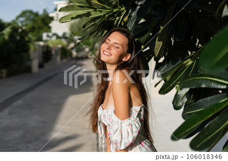 Young beautiful woman in a romantic dress with a floral print, and a pearl necklace bracelet, against the backdrop of tropical leaves Young beautiful woman in a romantic dress with a floral print, and a pearl necklace bracelet, against the backdrop of tropical leaves 106018346
