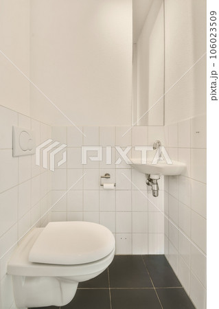 a white toilet in a small bathroom with black tiles on the floor and walls, there is a mirror above it a white toilet in a small bathroom with black tiles on the floor and walls, there is a mirror above it 106023509