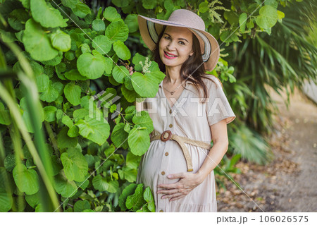 A serene and radiant pregnant woman after 40, surrounded by nature's beauty in the park, cherishing the journey of motherhood with a glowing smile 106026575