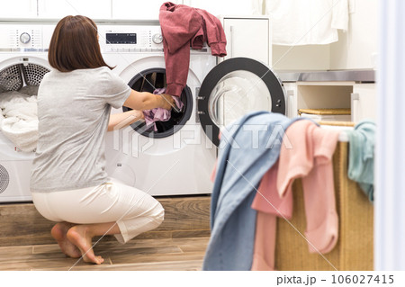 Woman Loading Dirty Clothes In Washing Machine For Washing In modern Utility Room Woman Loading Dirty Clothes In Washing Machine For Washing In modern Utility Room 106027415