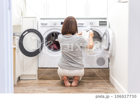 Woman Loading Dirty Clothes In Washing Machine For Washing In modern Utility Room 106027730