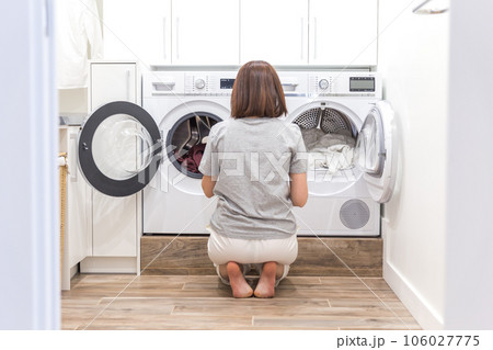 Woman Loading Dirty Clothes In Washing Machine For Washing In modern Utility Room 106027775