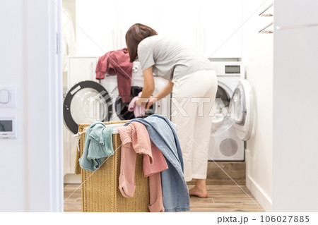 Young Woman loading washing machine and a Basket Full Of Dirty Clothes In Laundry Room 106027885
