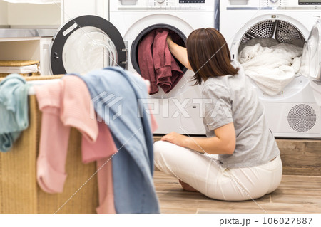 Woman Loading Dirty Clothes In Washing Machine For Washing In modern Utility Room 106027887