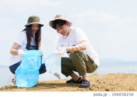 Group of Asian young people volunteer helping to collecting or picking up a plastic bottle garbage on the ground in park. Sustainability and environment conservation concept. 106036250