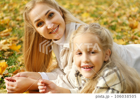 The family spends time together in the park. Girl and mother lie on a blanket, mother smiles and looks at the camera 106038505
