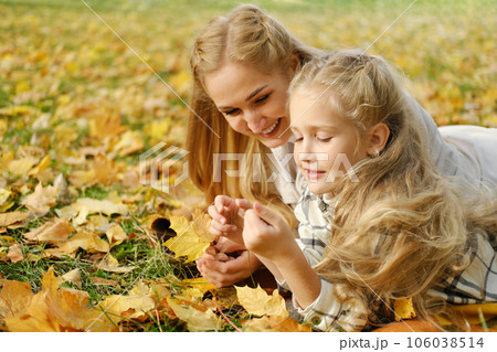 The Caucasian family has fun in the park. Girl and mother lie on a blanket and look at autumn leaves 106038514