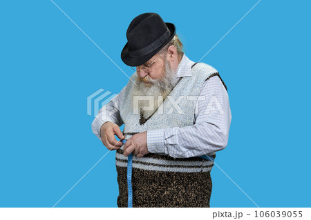 Senior man measuring waist with a blue tape. Lose weight concept. Isolated on vivid blue background. Senior man measuring waist with a blue tape. Lose weight concept. Isolated on vivid blue background. 106039055